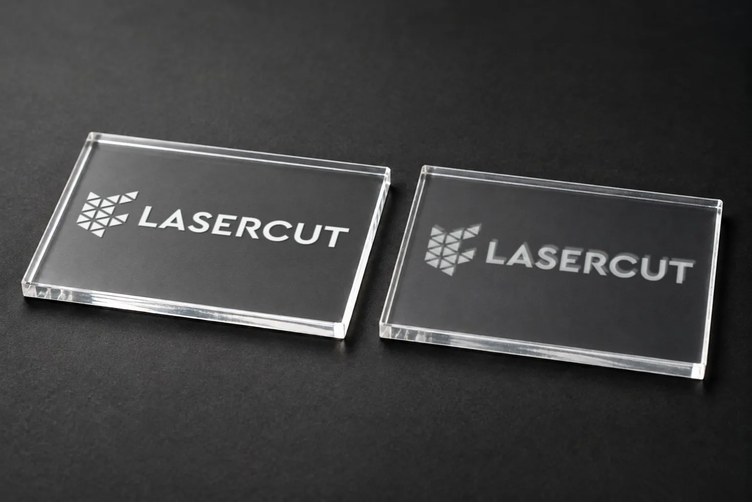 Две прозрачные акриловые пластины с лазерной гравировкой логотипа Lasercut: белый и менее контрастный рисунок на темном фоне.