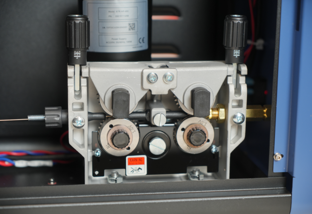 Механизм подачи проволоки (STR-WF00C) с роликами и этикеткой предупреждения.