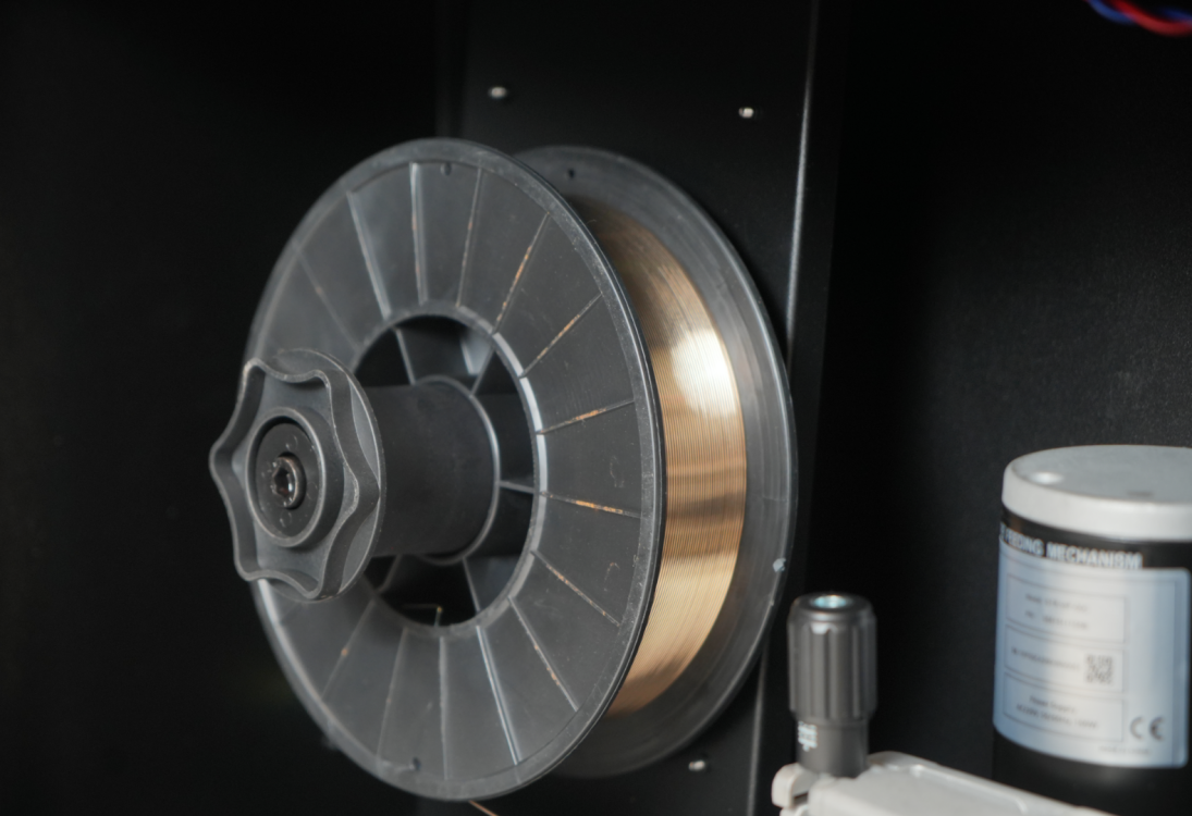 Шпулька с латунной сварочной проволокой внутри механизма подачи.