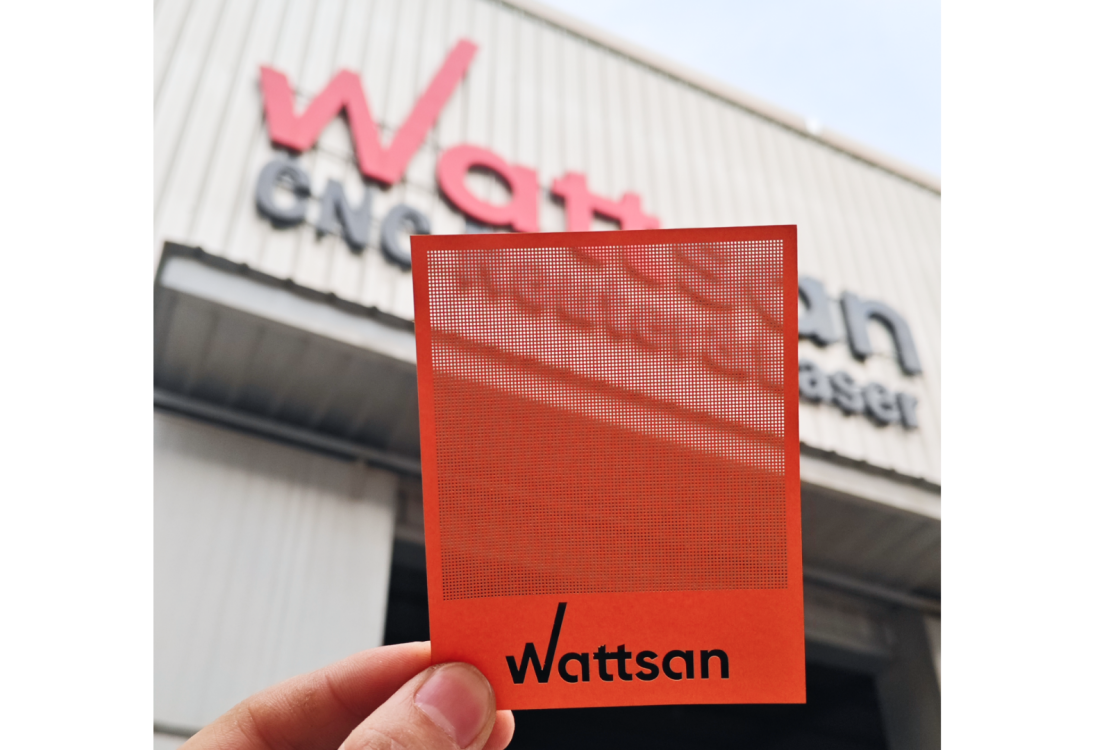 Рука держит красную перфорированную карту с логотипом "Wattsan", на фоне размытое здание Wattsan CNC Laser.