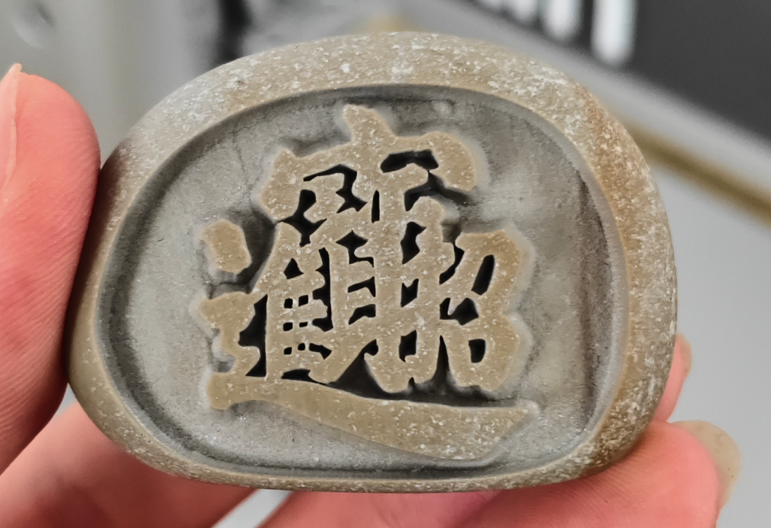 Рука держит бежевый каменный оттиск с вырезанными китайскими иероглифами в традиционном стиле