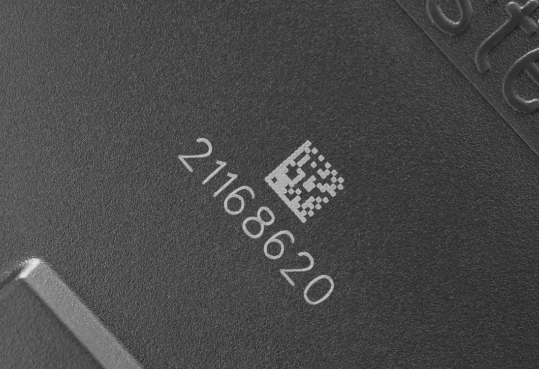 Крупный план тёмной поверхности с лазерной гравировкой числа "211688620" и маленького QR-кода