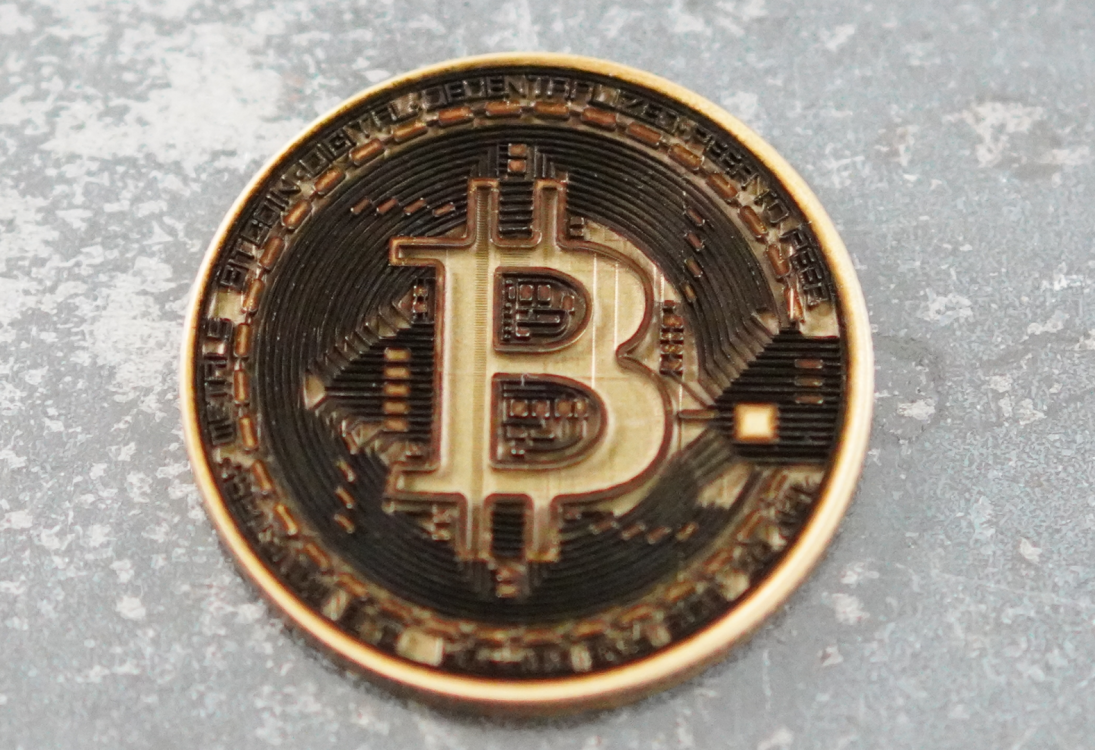 Крупный план монеты Bitcoin с детализированным рельефом и микроструктурой на металлическом фоне.