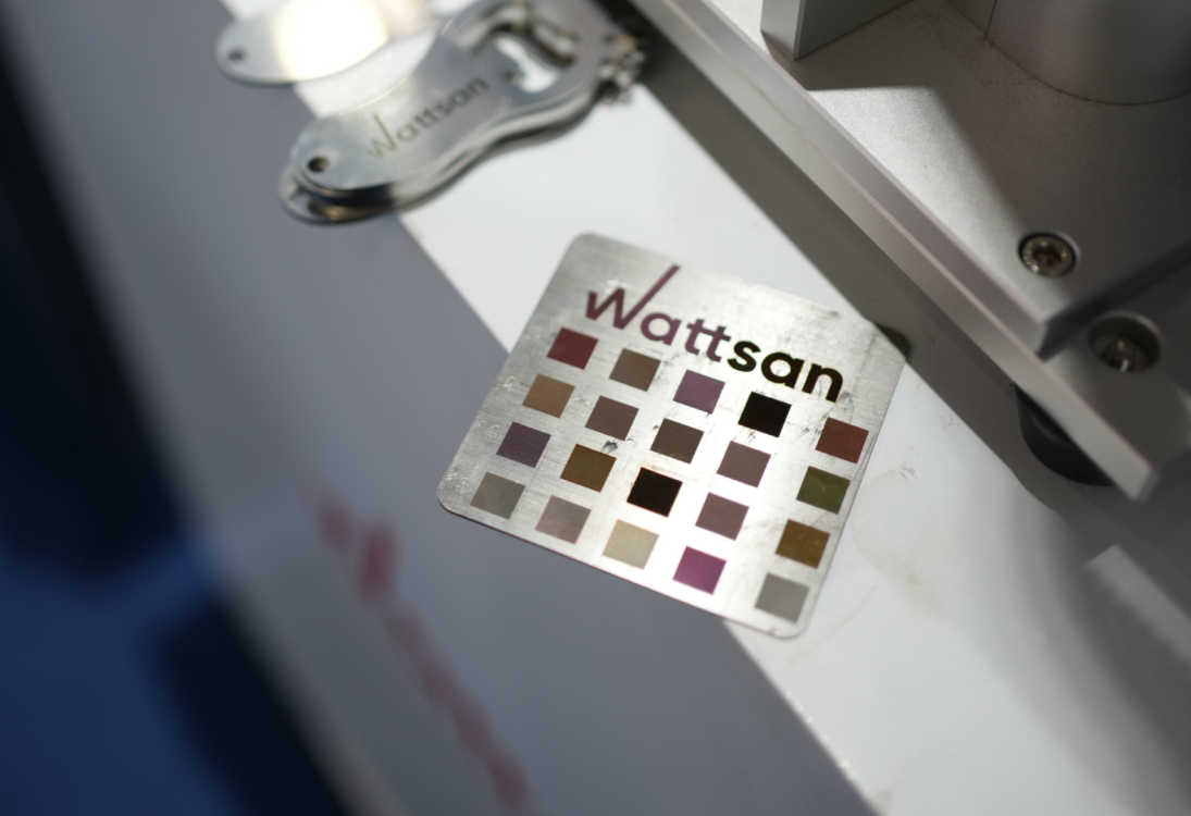Металлическая пластина с надписью "Wattsan" и сеткой цветовых квадратов в оттенках коричневого и фиолетового.